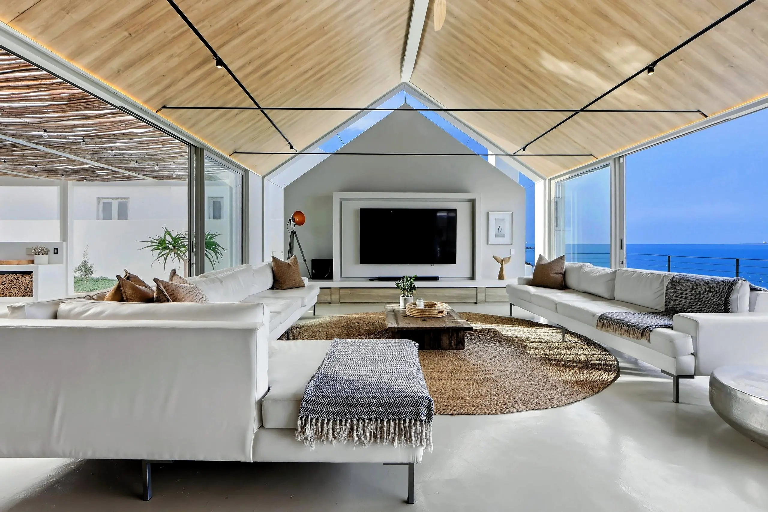 Gabled TV lounge with white sofas, a wall-mounted screen and sliding doors to the courtyard and sea