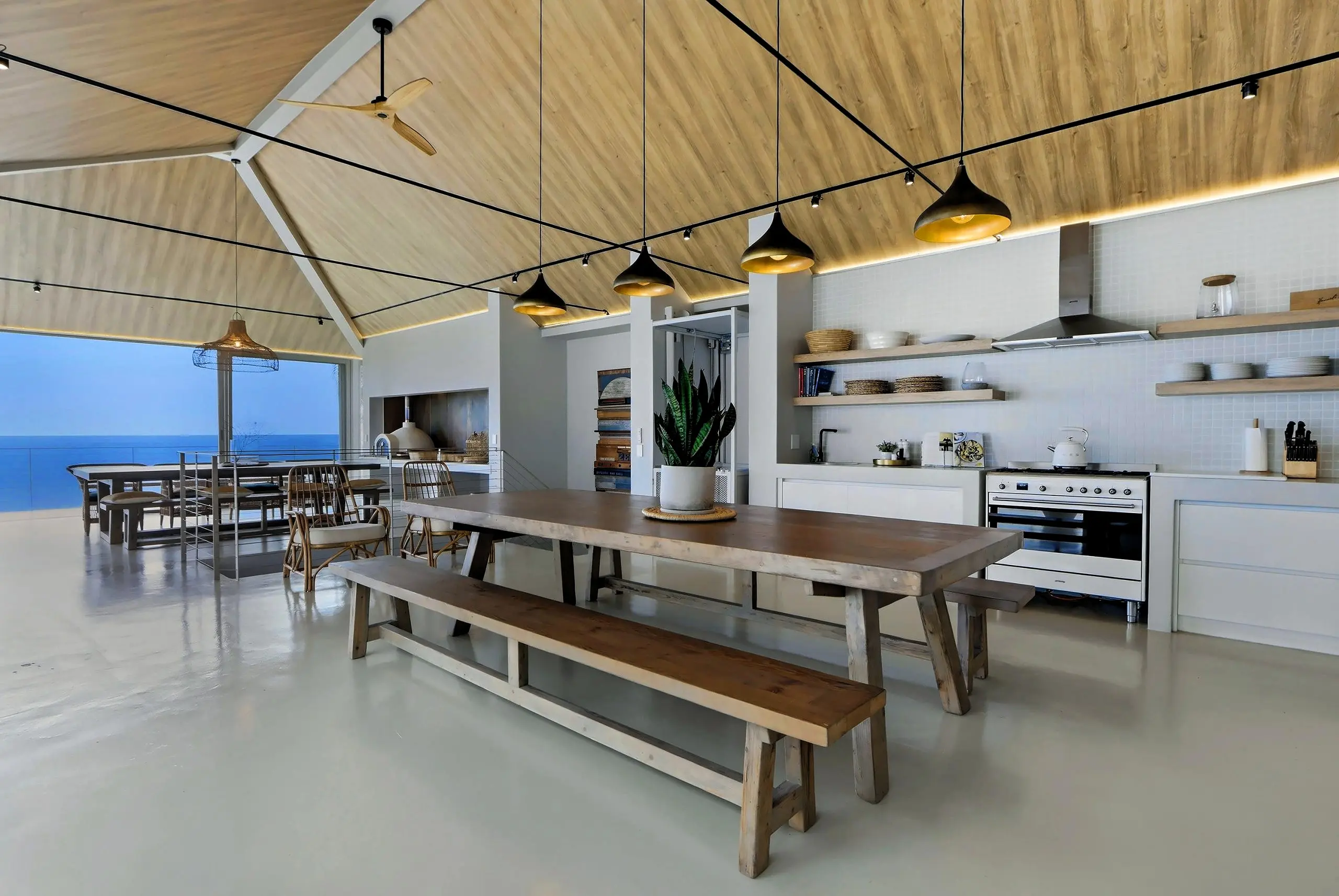Open kitchen with Smeg range, timber shelves, brass pendants and a long harvest table with benches