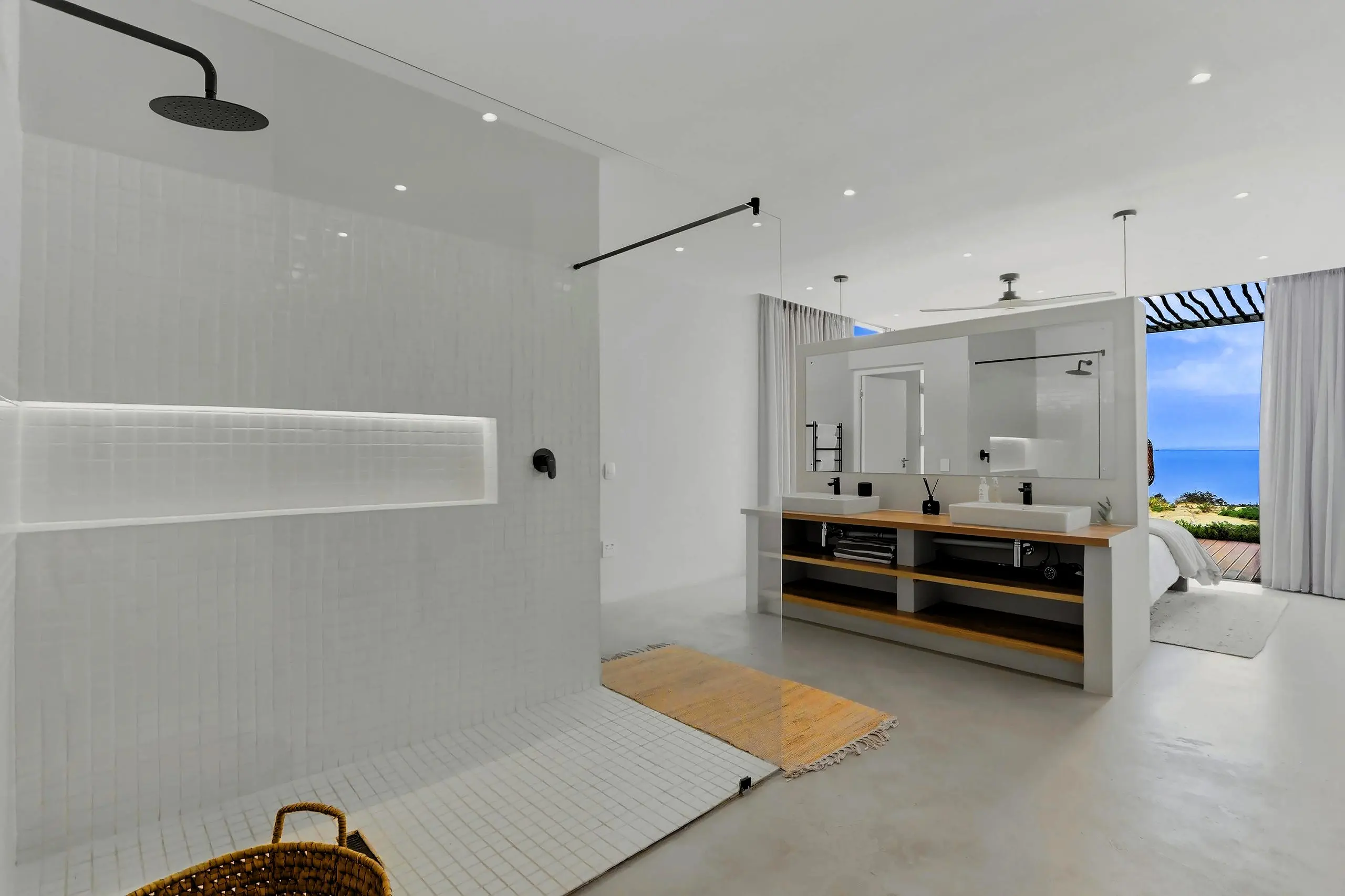 Large open bathroom with a tiled walk-in shower, double timber vanity and a view to the bedroom and sea