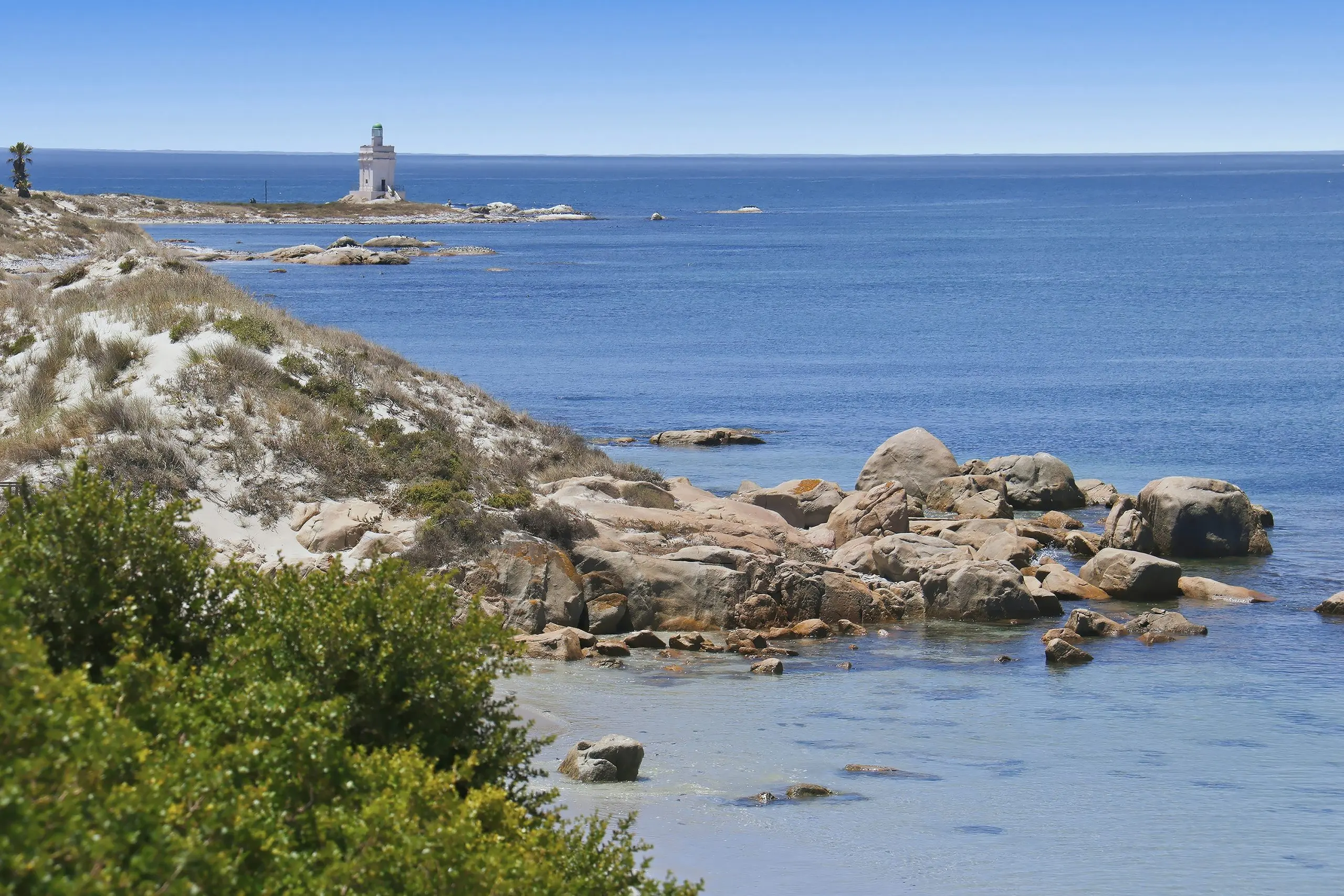 Rocky shoreline with turquoise shallows and a small lighthouse on the point