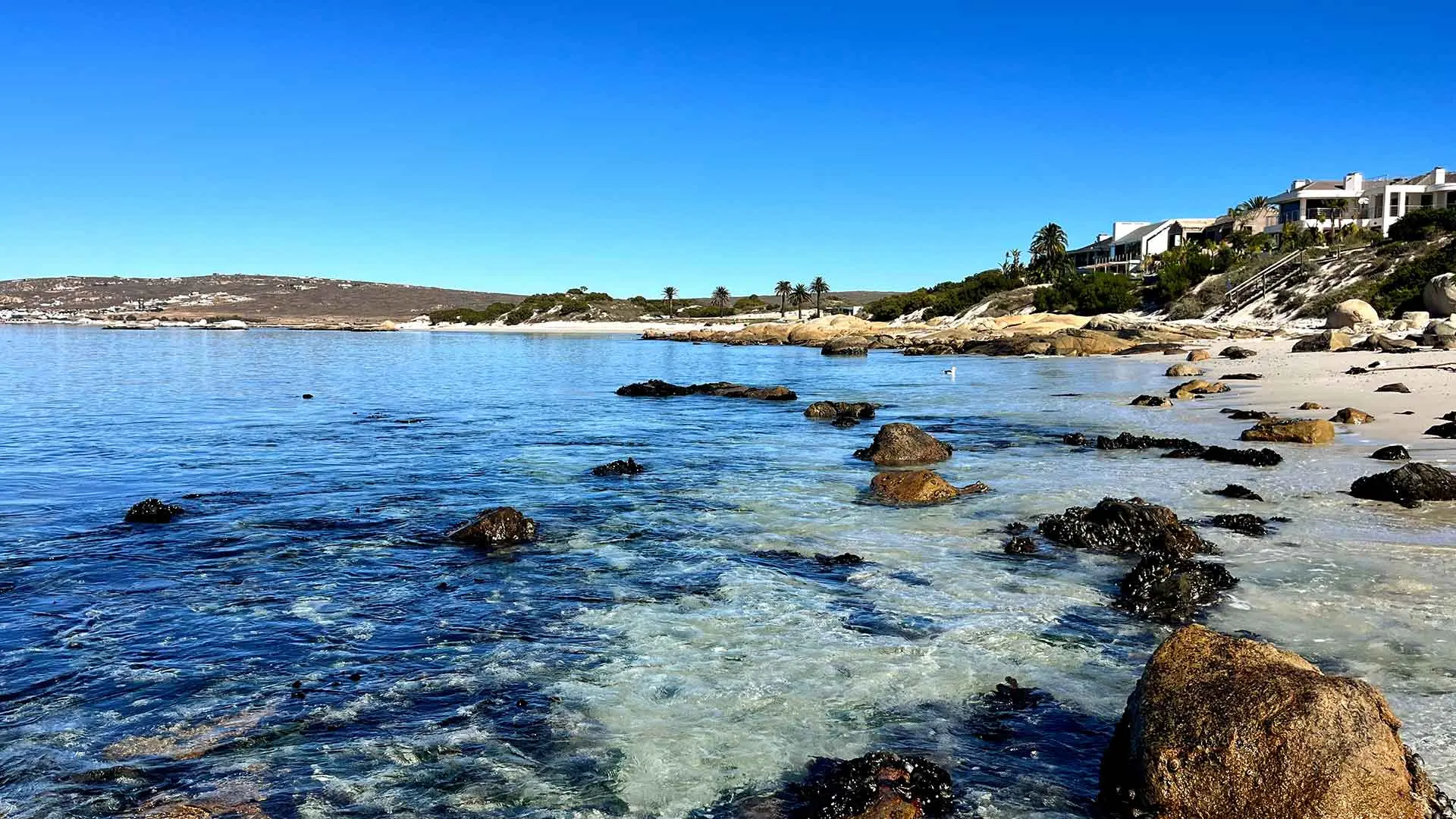 Rocky shallows of the calm bay with granite boulders, the villa on the shore behind
